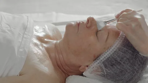 Cosmetologist's hand applying alginate mask to elderly woman's face in beauty Video stock 337123700