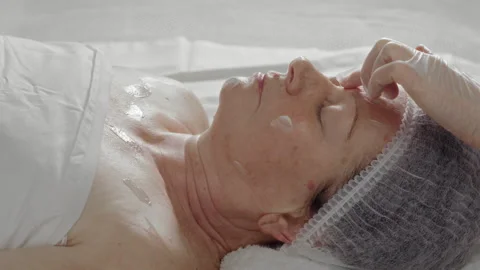 Cosmetologist's hand applying cream to the face of an elderly woman in a beauty Stock-Footage 337119808