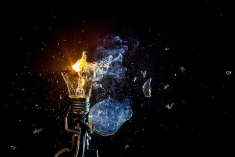 Cosmic explosion of a burning light bulb with flying splinters and smoke on a Stock Photos