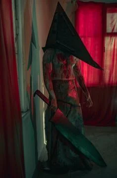 Cosplayer in the image of executioner stands in dark room with knife 스톡 사진