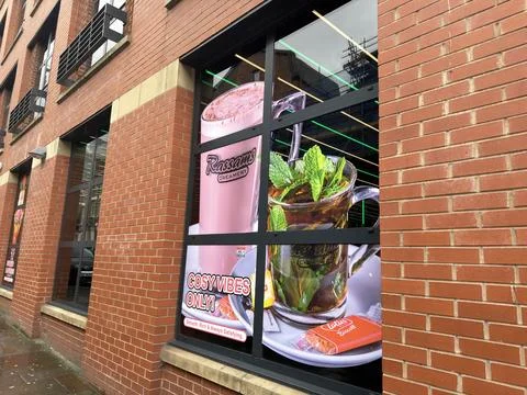 Cosy vibes cafe window with mint tea and pink milkshake poster on red brick.. Stock Photos