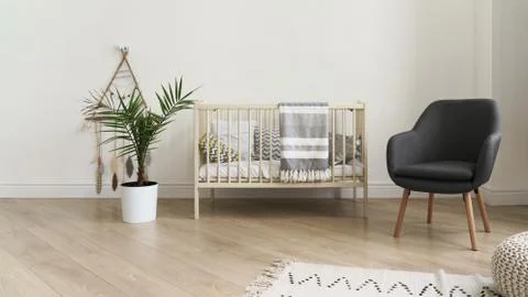 Cot bed and modern gray chair in baby bedroom Stock Photos
