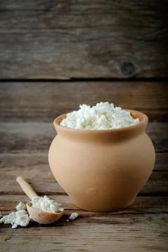 Cottage cheese in brown rustic clay pot and wooden spoon. 库存照片