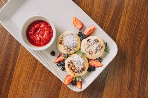 Cottage cheese pancakes with strawberries on rectangular plate with sauce on Stock Photos