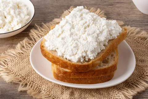 Cottage cheese spread on slices of bread on a plate placed on a wooden tabl.. Stock Photos