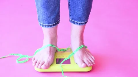 Coucasian bare feet standing on scale to measure weight,pink background. Control Stock Footage 247969192