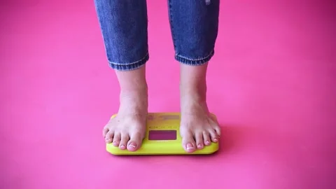Coucasian bare feet standing on scale to measure weight,pink background. Control Stock Footage 248070992