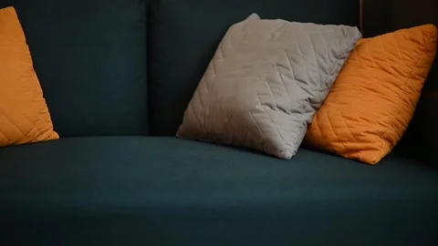 A couch with gray and orange pillows is styled in a living room. The couch is 스톡 동영상 336778703