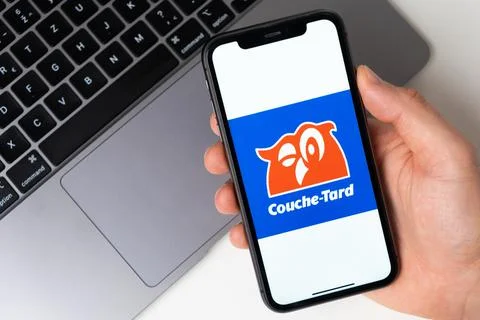 Couche Tard the application is open in the smartphone. The man is holding a Stock Photos