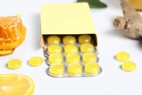 Cough drops in blister with ginger root, lemon slice and honeycomb on white b Stock Photos