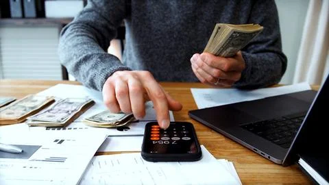 Counting dollar bills and checking totals on phone Stock Photos