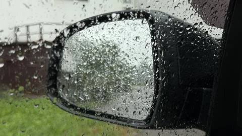 Countless raindrops covering a car window, looking out toward the side mirror Stock Photos