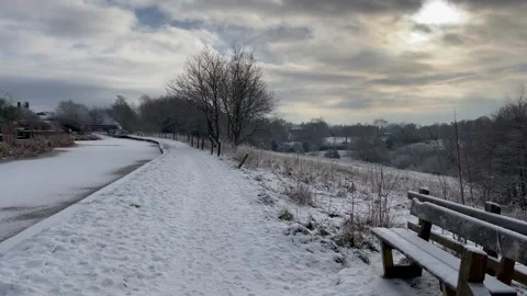 Country bench alongside snow covered canal moody sky Stock Footage 297413345