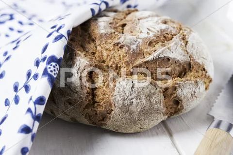 Country bread partially hidden under a floral-patterned cloth Stock Photos