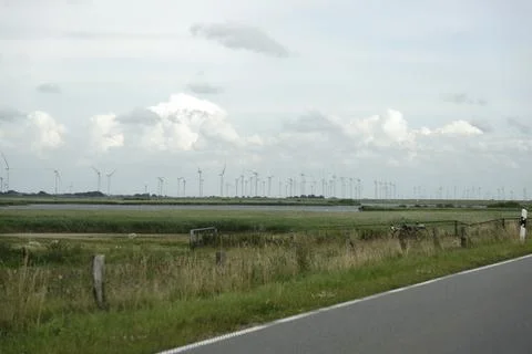 Country road beside fields with distant wind farm of many turbines. Stock Photos