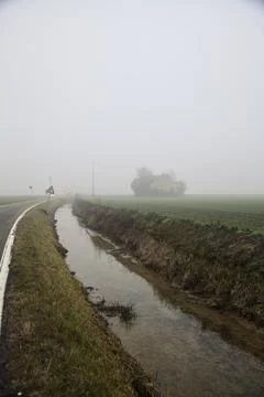 Country road bordered by fields and a channel with an abandoned house in th.. Stock Photos