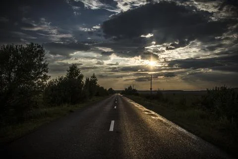 Country road at sunset with dramatic clouds and sunbeams in the background Stock Photos