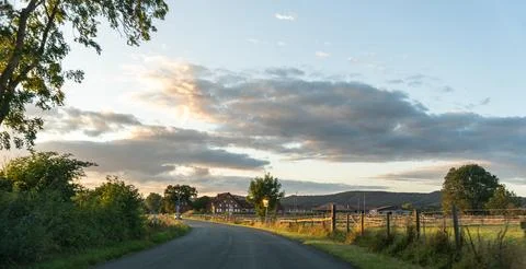 Country road at sunset with dramatic clouds over a rural village, asphalt road Stock Photos