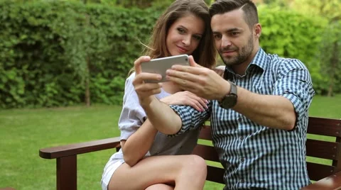 Coupl sitting on the bench and taking selfie picture. They are kissing Stock Footage 51441908