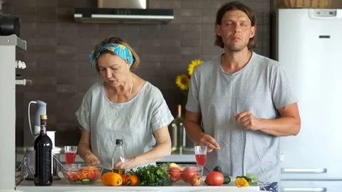 A couple with an age difference prepare the salad in the kitchen, they relax to Stock Footage 96488985