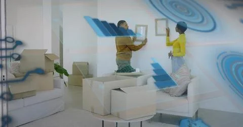 Couple aligning small picture frames on living room wall, with moving boxes a Stock Photos