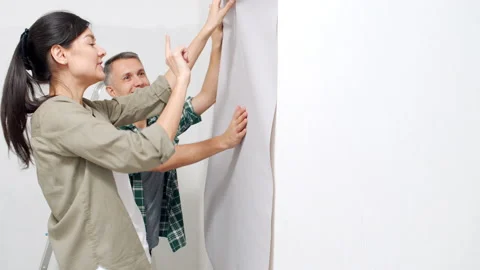 Couple applying roll of wallpaper to wall and discussing renovation details Stock Footage 143540752