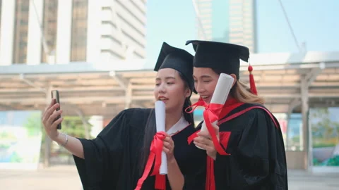 Couple of Asian beautiful women with graduation gown use mobile phone selfie Stock Footage 143482660