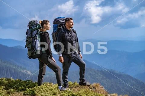 The couple with backpacks enjoying on a beautiful mountain landscape backgrou Stock Photos