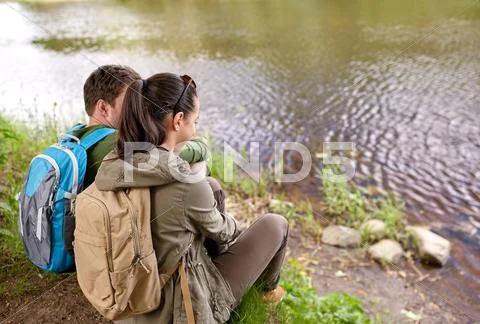 Couple with backpacks sitting on river bank Stock Photos