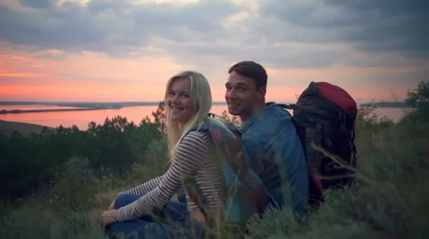 Couple with backpacks smiling looking at camera sitting on hill Slow motion Stock Footage 68117252