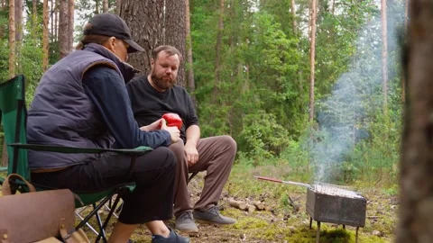 Couple barbecuing meat on a grill during a forest picnic Stock Footage 327135392
