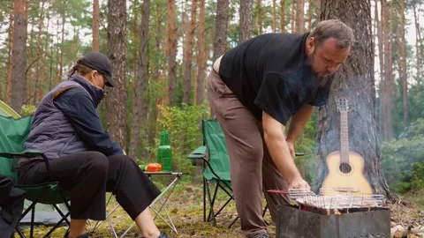 Couple barbecuing meat on a grill during a forest picnic Stock Footage 327135468