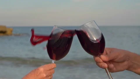 A couple on the beach toast with two red wine glasses and the wine sloshes. Stock Footage 135350738