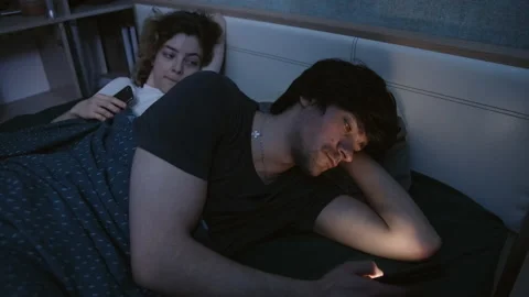 The couple in bed, the guy turned away from the woman and looks at the phone Vidéo 197365091