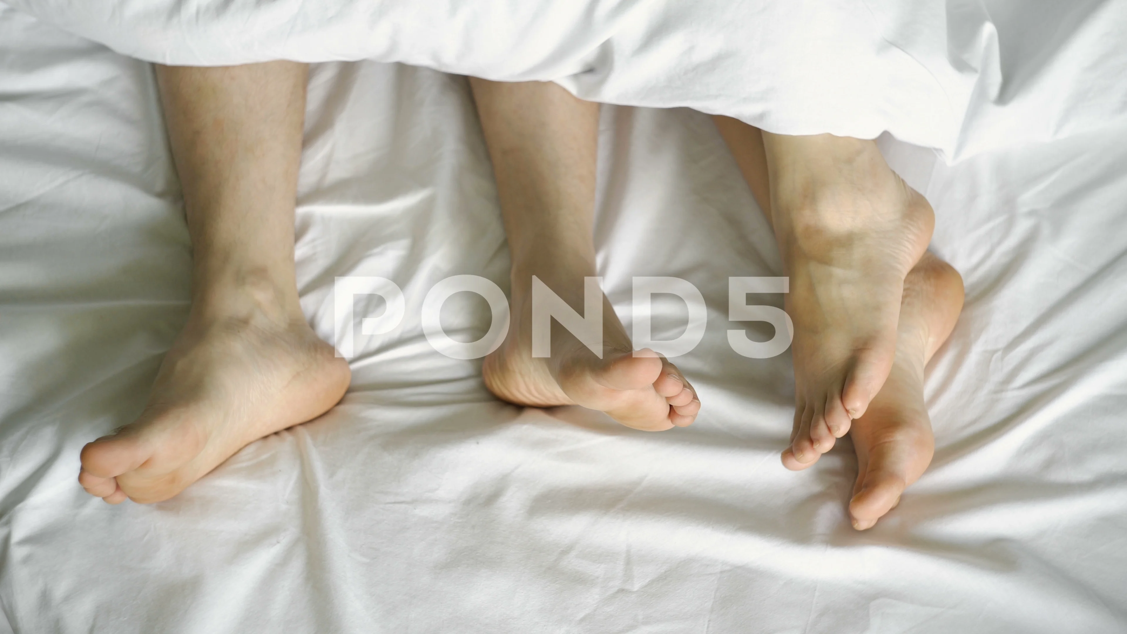 couple in bed making love. male and female legs top view, white linens.  sex, 4k