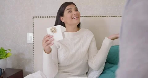 Couple in bed, robed man giving gold-bow box, woman opening, gasping, hugging Stock Footage 345589154