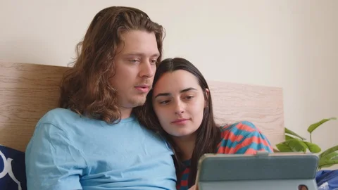 Couple in bed snuggling up and being entertained by the smart tablet. - slow Stock Footage 129461344