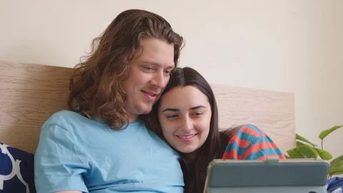 Couple in bed snuggling up and being entertained by the smart tablet. Stock Footage 129895096