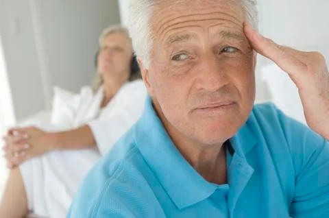 Couple in bedroom, thinking man in foreground, woman listening to music with Stock Photos