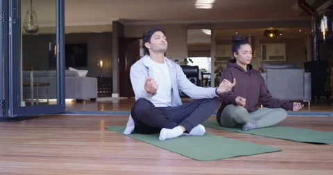 Couple bringing hands to mudra, meditating on green mats at home near folding Stock Footage 339678911