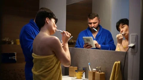 Couple brushing teeth in the bathroom and looking on tablet 스톡 동영상 73753703