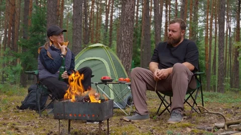 Couple camping in forest drinking beer and talking by campfire Video stock 327134869