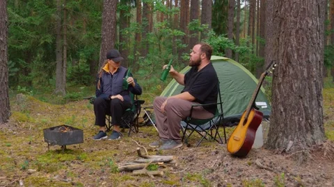 Couple camping in forest drinking beer and talking by campfire Stock Footage 327134947