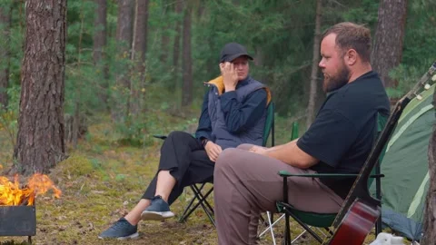 Couple camping in forest drinking beer and talking by campfire Vidéo 327134982