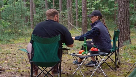 Couple camping in forest drinking beer and talking by campfire Stock Footage 327135118