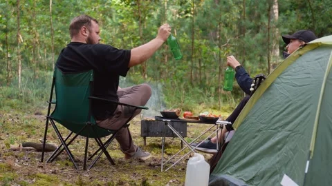 Couple camping in forest drinking beer and eating outdoors Stock Footage 327136036