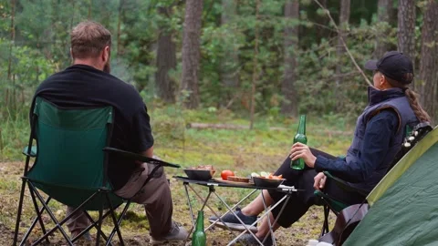 Couple camping in forest drinking beer and eating outdoors Stock Footage 327136054