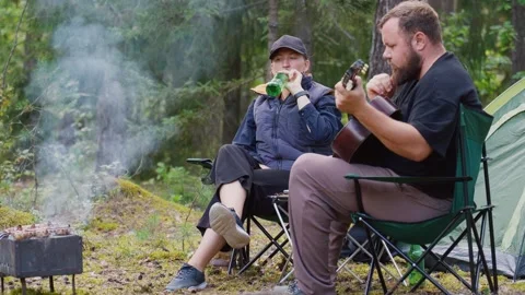 Couple camping in forest with man playing guitar Stock Footage 327136707