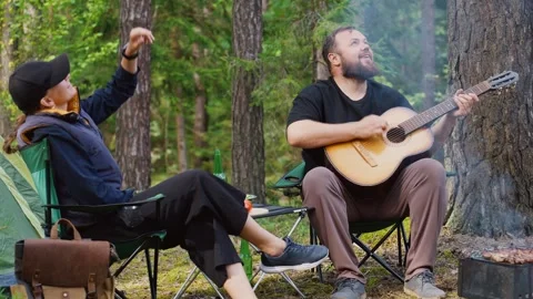 Couple camping in forest with man playing guitar Stock Footage 327136770