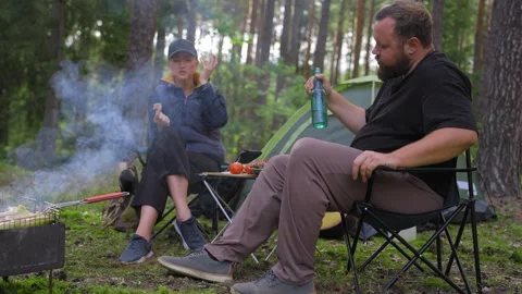 Couple camping in forest talking and grilling food Stock Footage 327132345